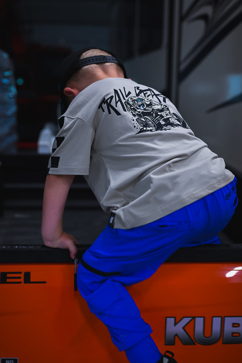 A person wearing a light gray graphic t-shirt and bright blue pants climbing onto an orange vehicle, viewed from behind.